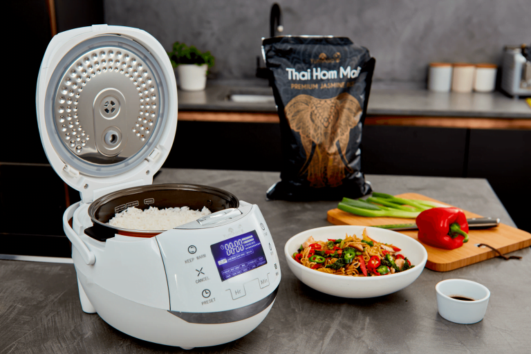 Yum Asia Sakura rice cooker with lid open in white with Thai Hom Mali jasmine rice in the background
